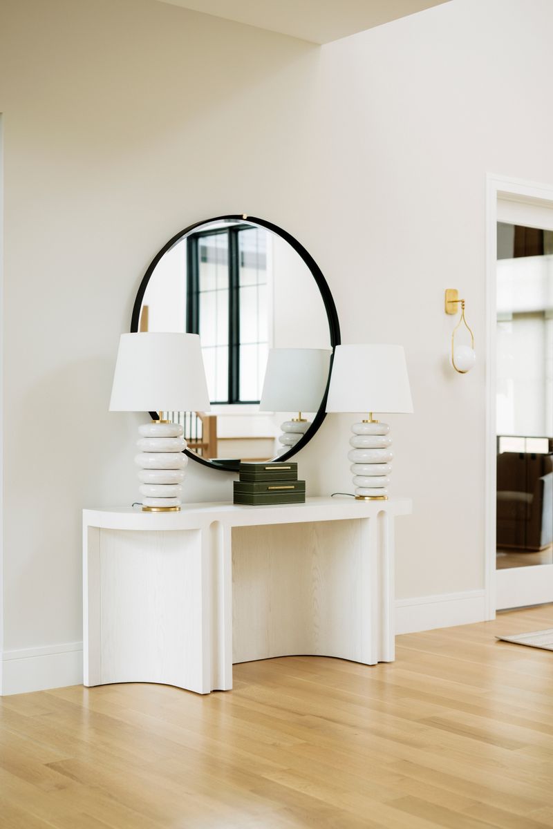 A bright entry in West Des Moines with a round black mirror over a curved white oak console table.