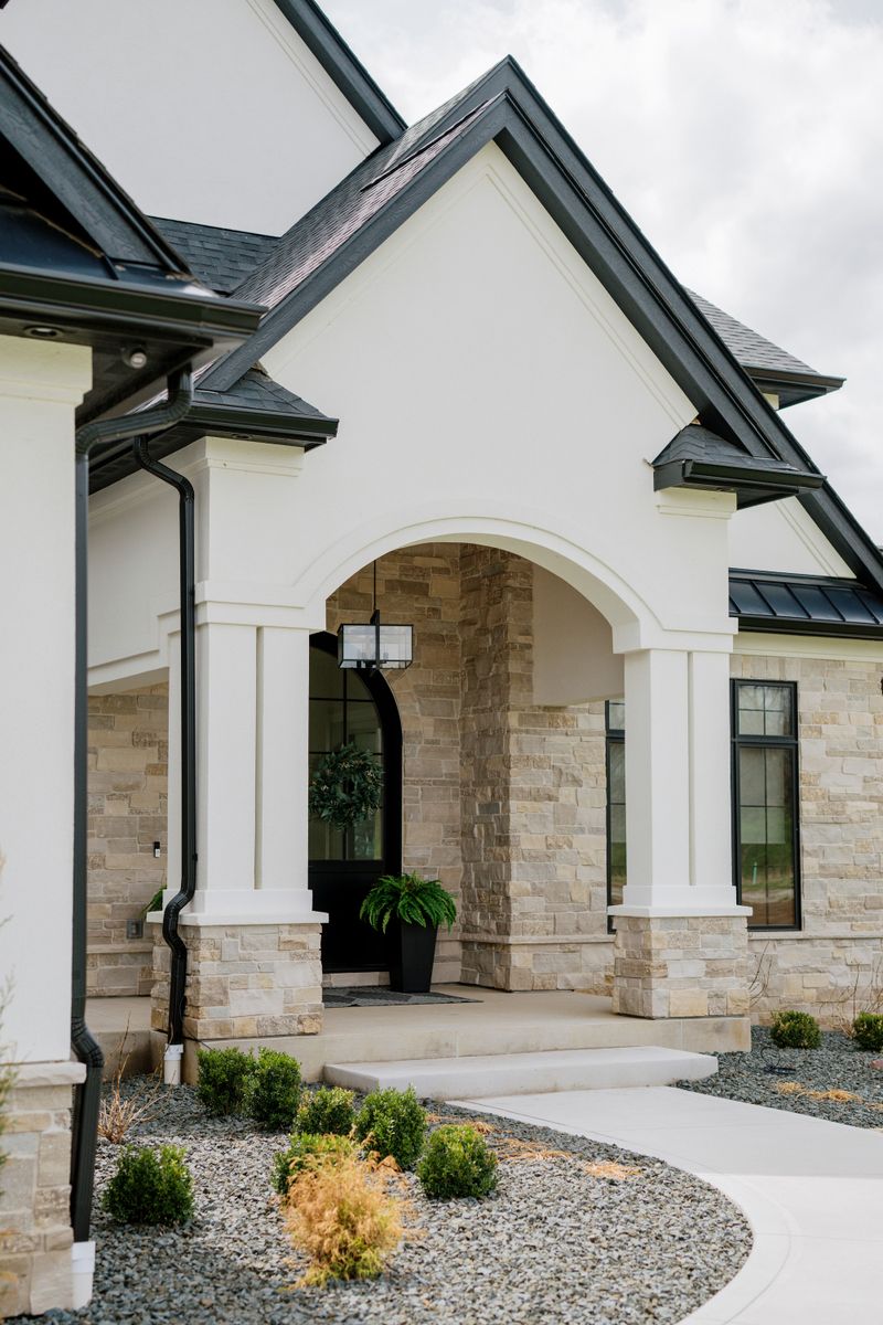 A white stucco exterior in West Des Moines with a black arched front door set in limestone.