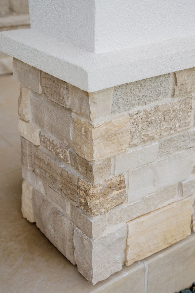 A limestone porch column in West Des Moines with a smooth white cast stone cap over rough cut cream stone.