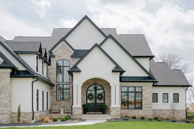 A white stucco and stone exterior in West Des Moines with a black arched double front door under a steep gable.