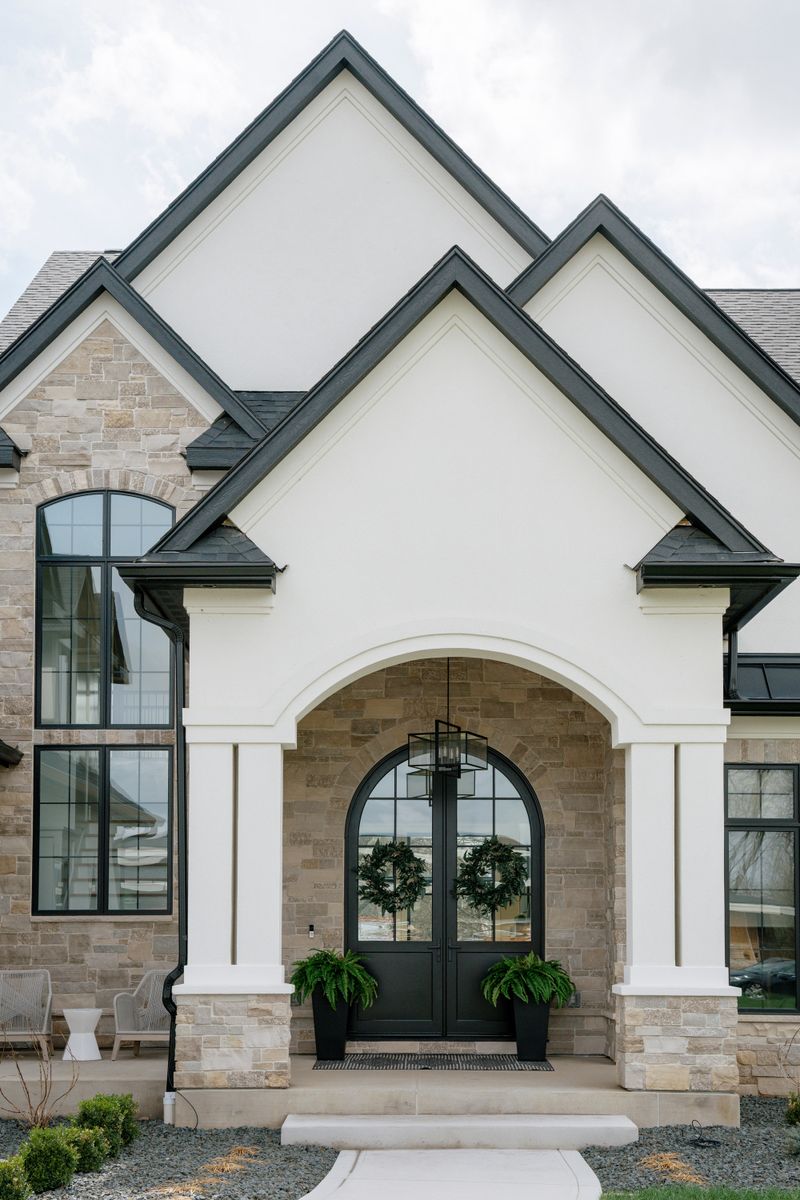 A white stucco home exterior in West Des Moines with a black arched double front door under a stone entry.