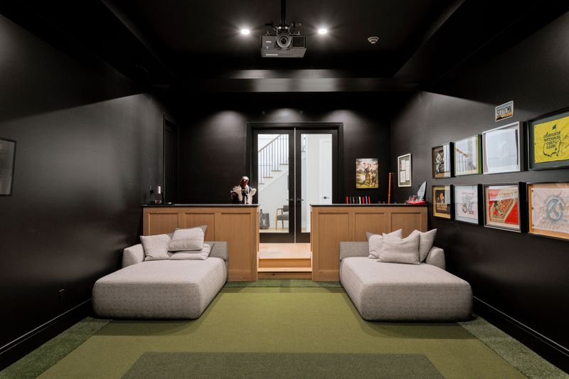A black golf simulator room in West Des Moines with white oak paneled half walls and green turf flooring.
