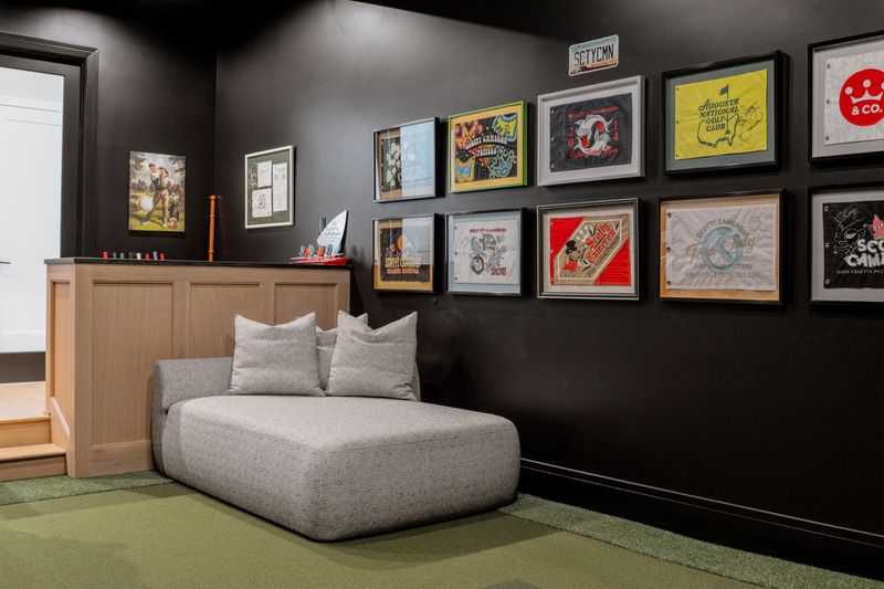 A golf simulator room in West Des Moines with black walls and a white oak half wall over green turf flooring.