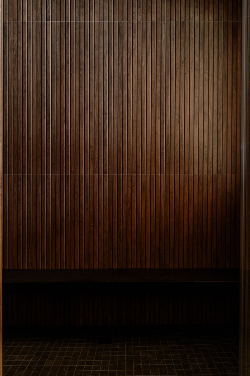 A Sauna in West Des Moines with a full height dark wood tile wall above a built in bench.