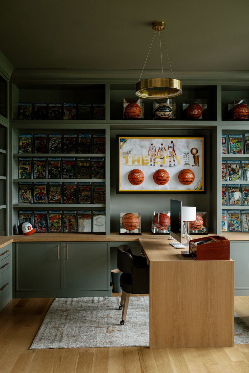 A green home office in West Des Moines with built-in comic book display shelves and a white oak desk.
