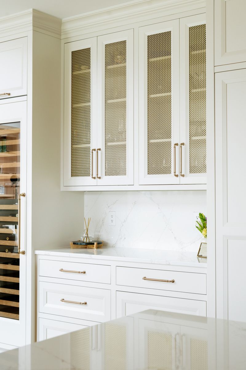 A white kitchen in West Des Moines with brass mesh cabinet fronts above a veined marble backsplash.