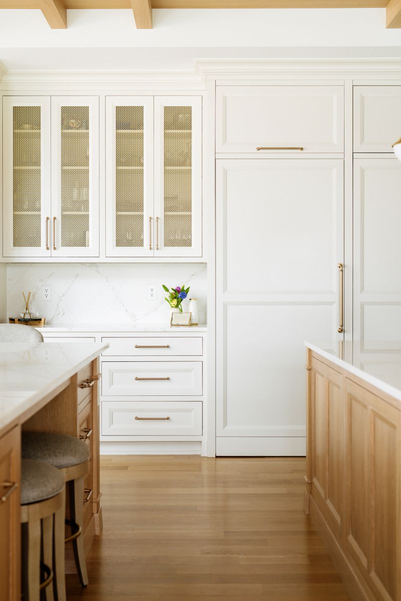 A creamy white kitchen in West Des Moines with brass mesh cabinet doors above a marble backsplash.
