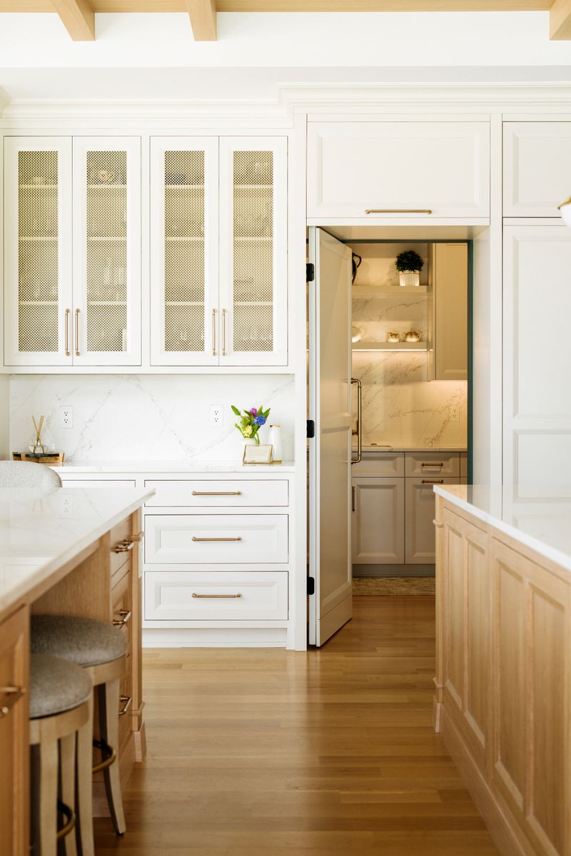 A white kitchen in West Des Moines with brass mesh cabinet doors beside a hidden pantry door.