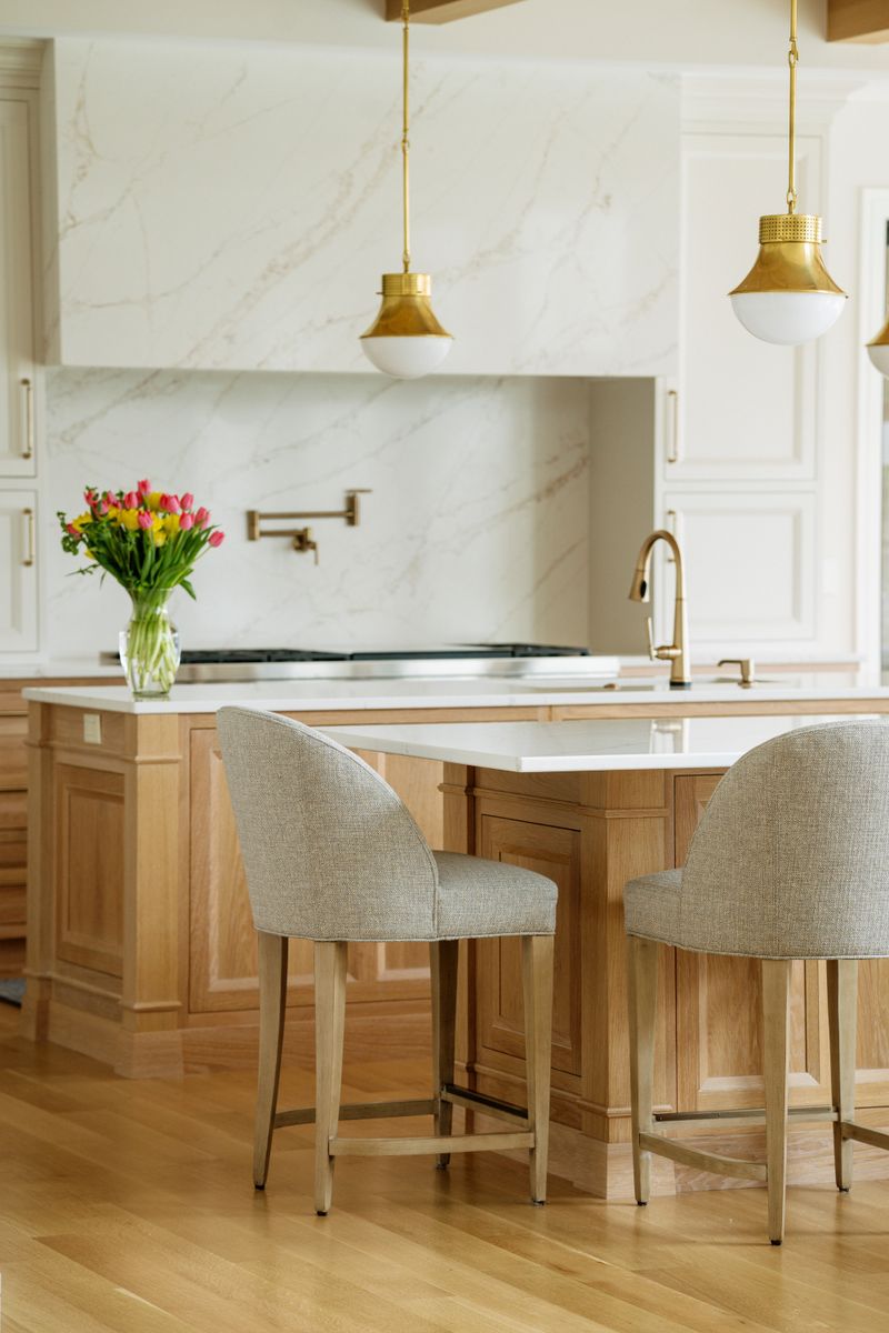 A cream kitchen in West Des Moines with a marble slab hood over the range and a white oak island.