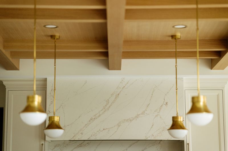 A West Des Moines kitchen with brass globe pendants hanging below a white oak beamed ceiling.
