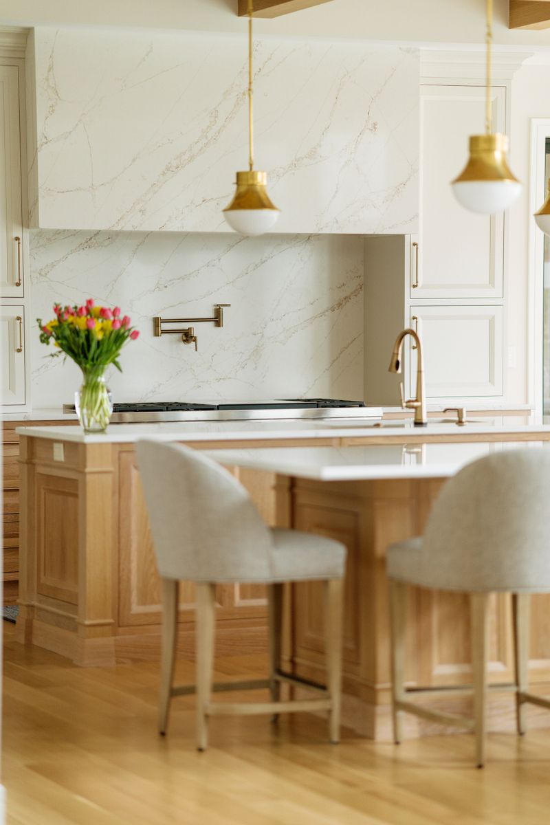 A cream kitchen in West Des Moines with a marble-clad hood over the range and a white oak island.