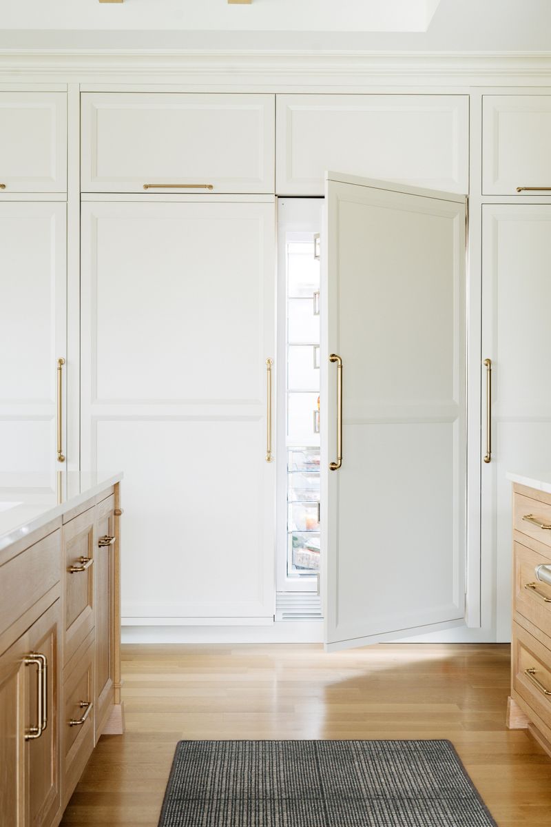 A white kitchen in West Des Moines with a panel front refrigerator hidden behind brass pull cabinet doors.