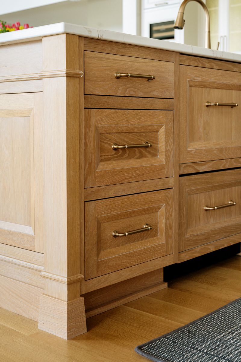 A white oak kitchen island in West Des Moines with brass pulls on the drawers and a marble countertop.