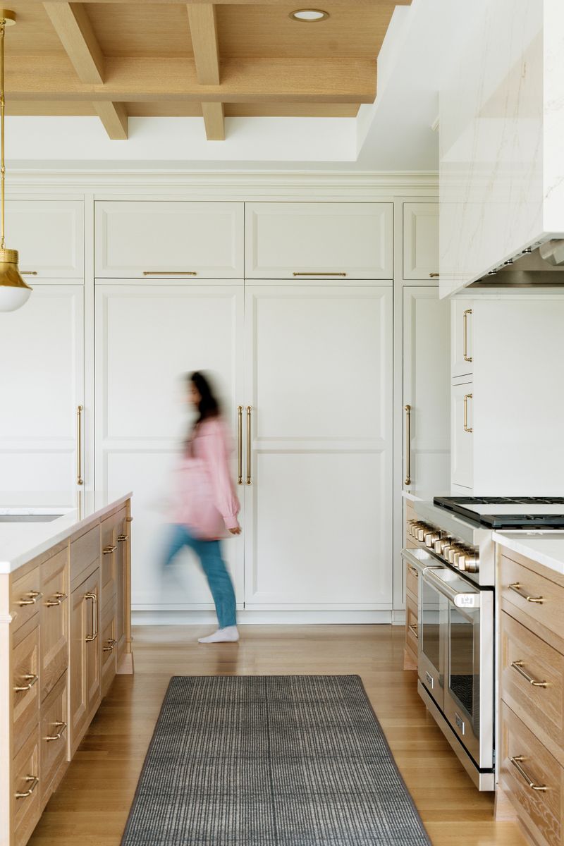 A cream kitchen in West Des Moines with white oak cabinets and brass pulls beside a stainless double range.