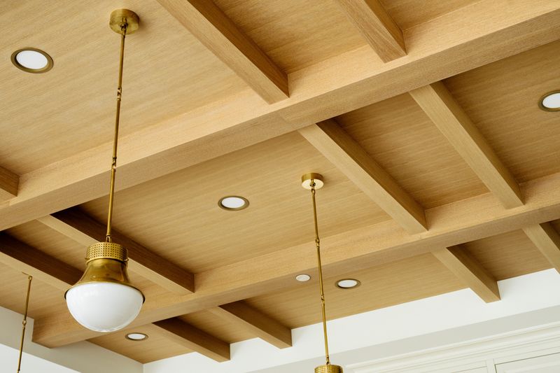 A West Des Moines kitchen with a coffered white oak beam ceiling and brass pendants hung from it.