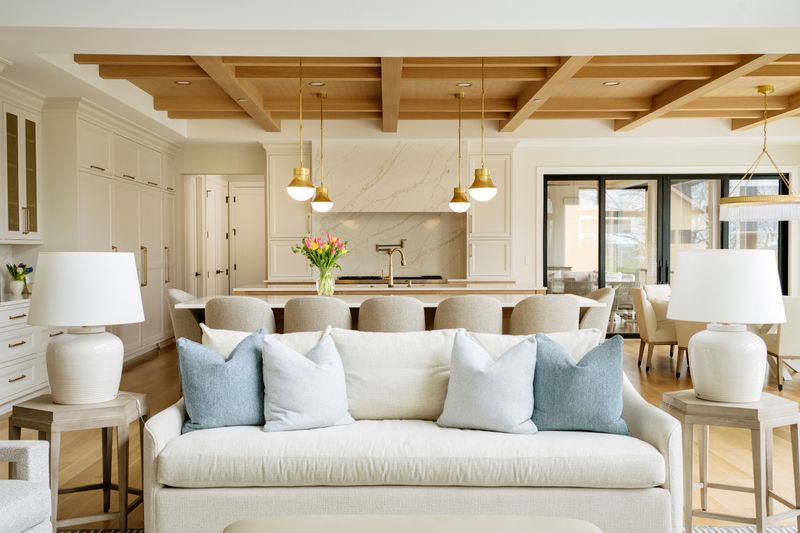 An open living room in West Des Moines with a white oak beamed ceiling above a cream sofa and light oak floors.