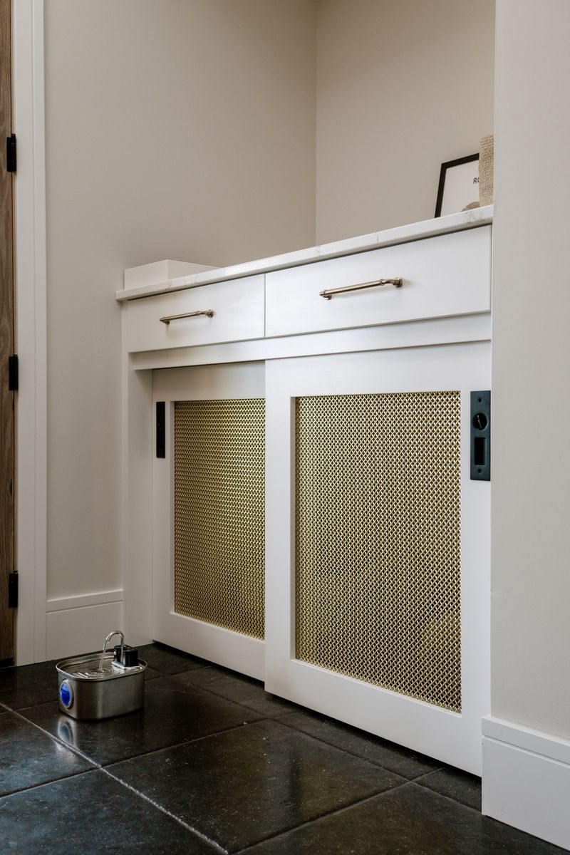 A mudroom in West Des Moines with brass mesh sliding doors on white cabinets over dark stone tile floors.