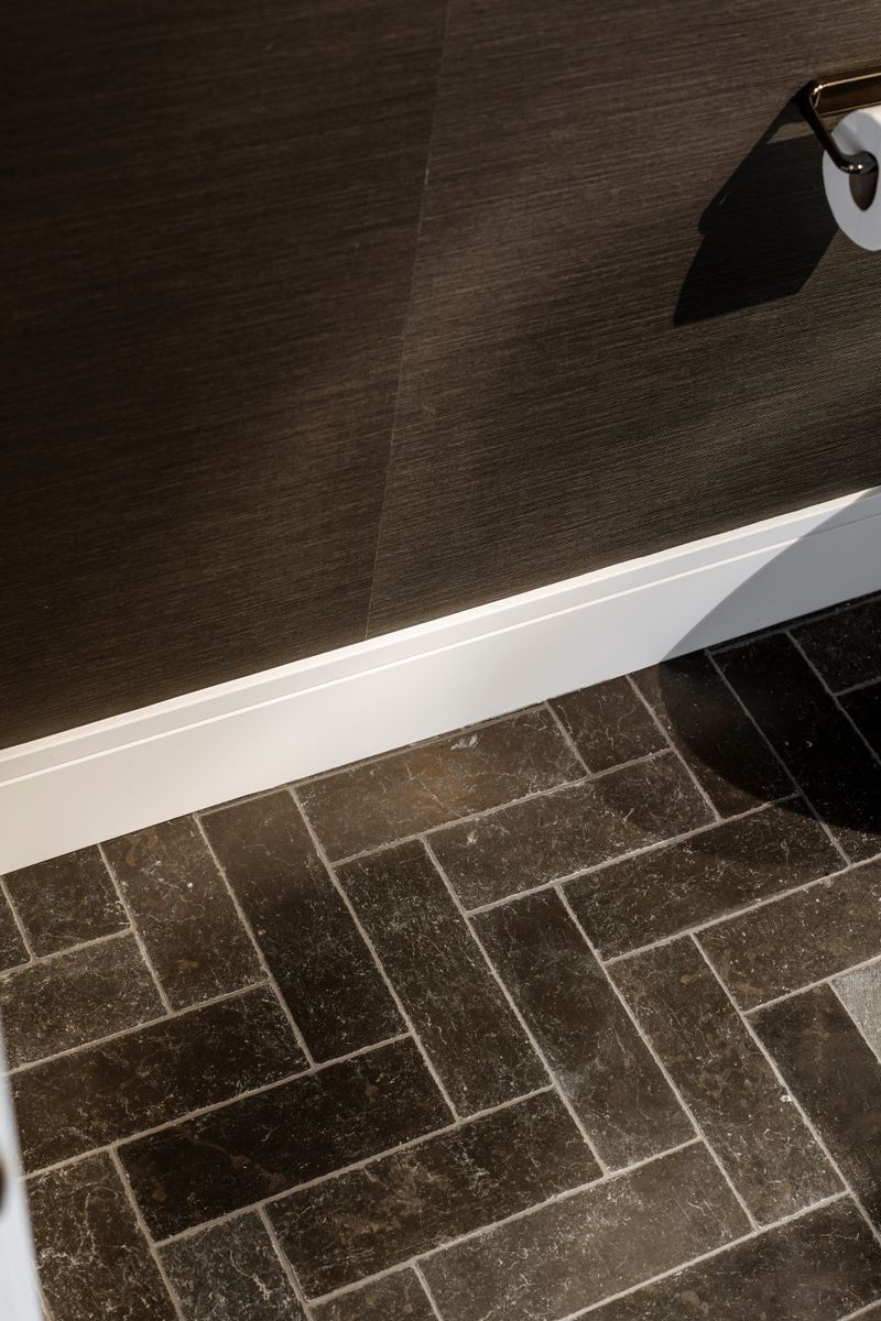 A powder room in West Des Moines with a brown herringbone stone floor meeting textured grasscloth walls.