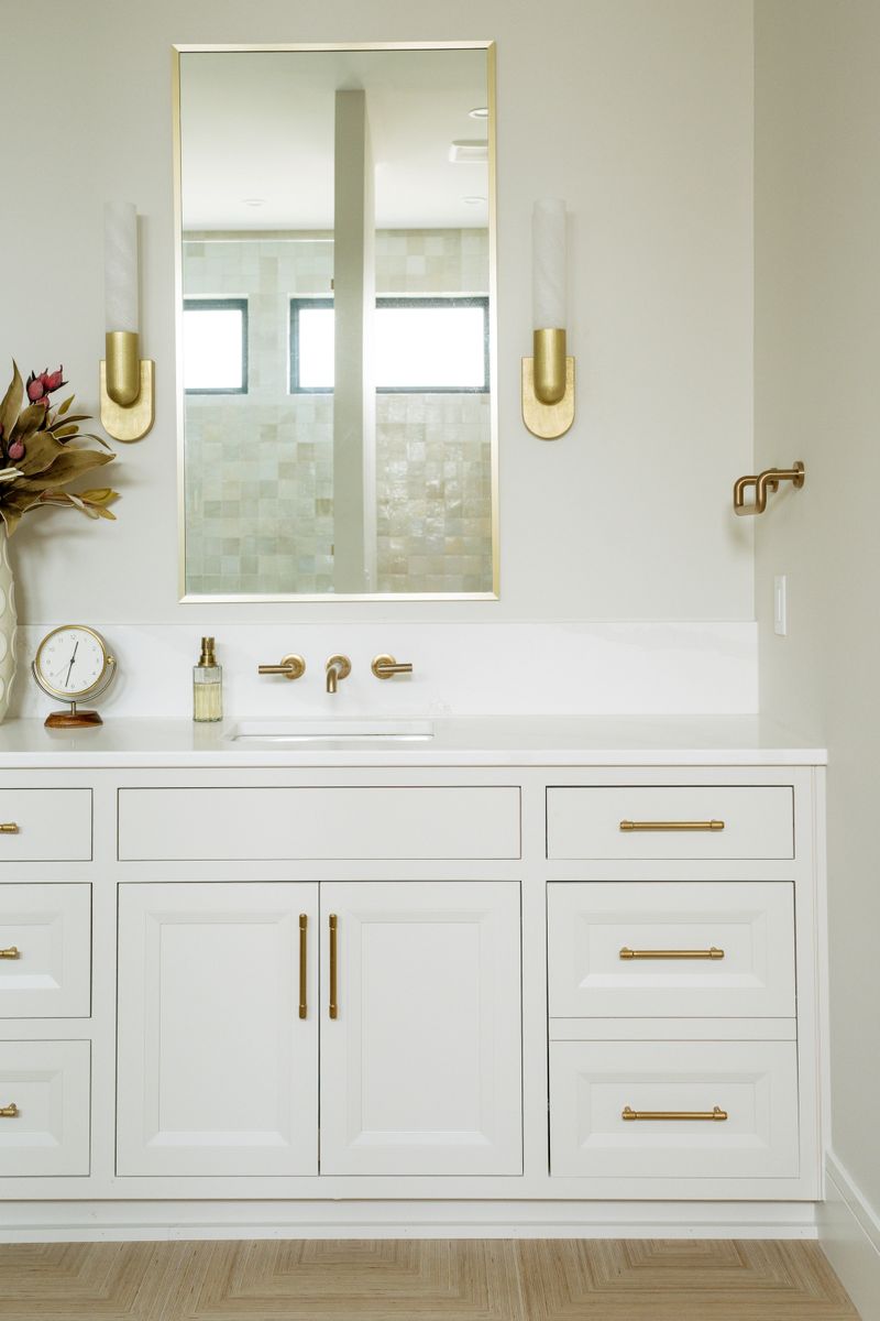 A primary bath in West Des Moines with brass wall mount faucets over a white vanity and quartz counter.