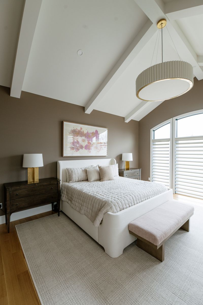 A primary bedroom in West Des Moines with taupe walls under white beams and a fluted drum pendant.