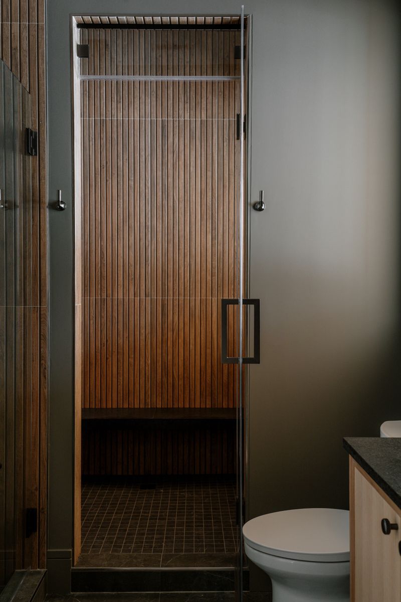 A cedar slat sauna in West Des Moines with a glass door and a black bar pull against a deep green wall.