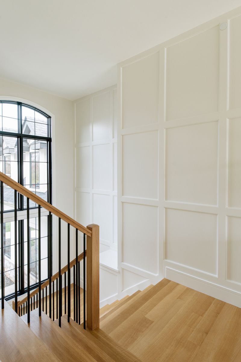 A stair landing in West Des Moines with white paneled walls and a white oak railing over black metal spindles.