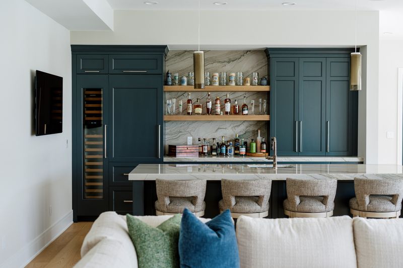 A wet bar in West Des Moines with deep teal cabinets built around a tall glass-front wine fridge.