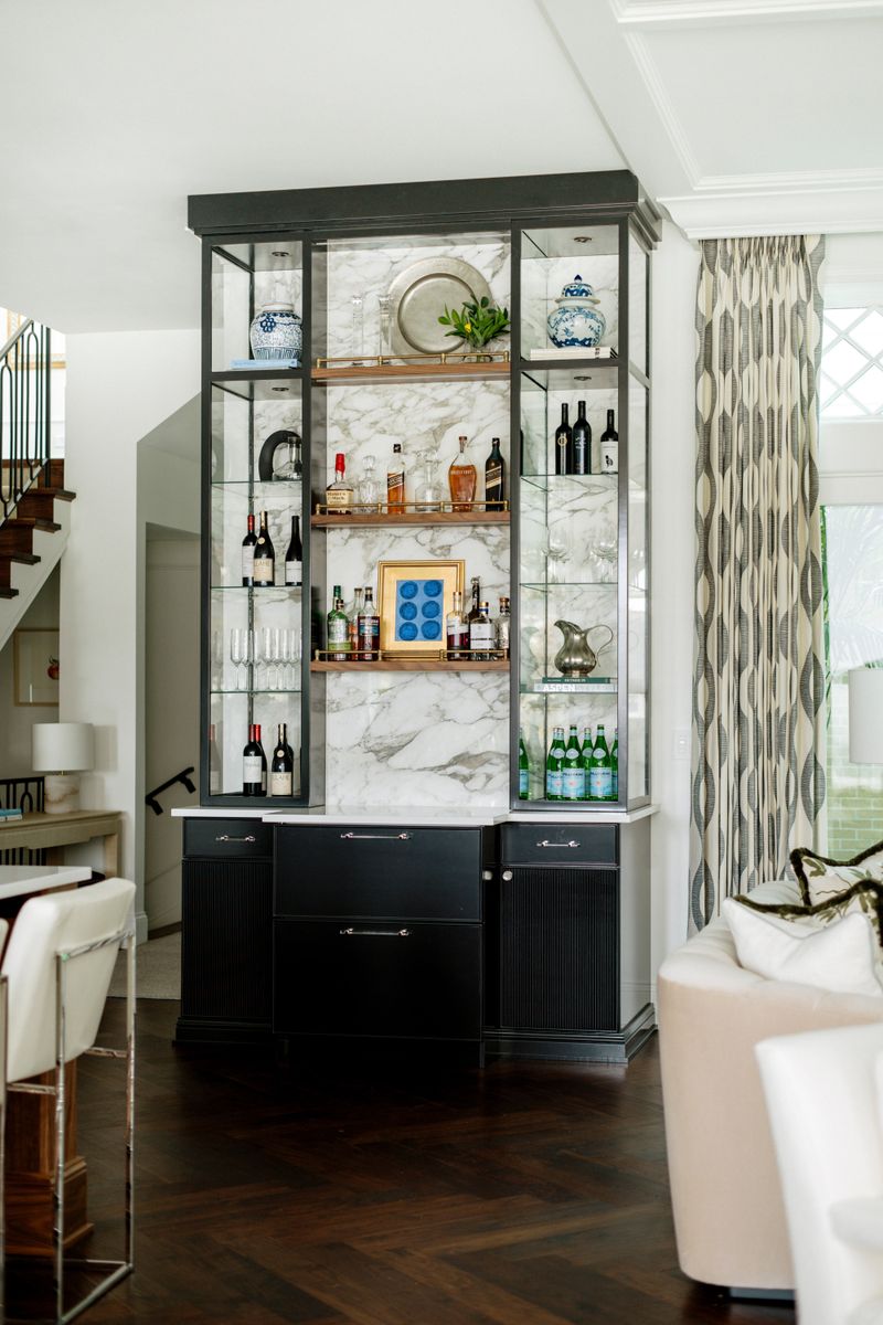 A built-in bar in Des Moines with black glass cabinets against a marble backsplash and walnut shelves.