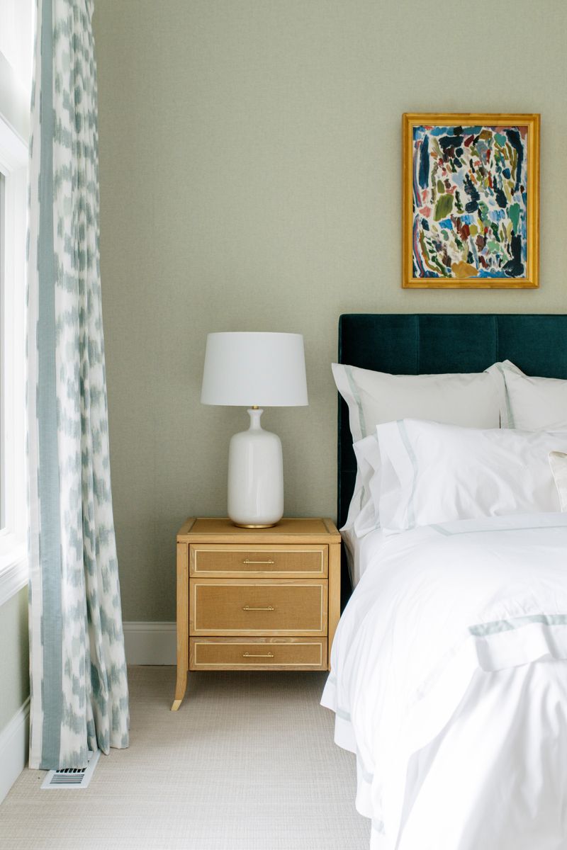 A sage green bedroom in Des Moines with a teal velvet headboard beside a light oak nightstand.