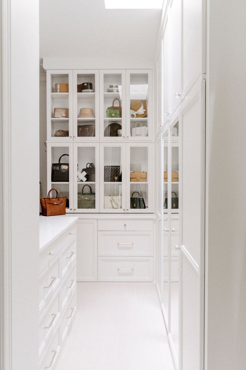 A white walk in closet in Des Moines with glass front cabinets built for handbag storage above white drawers.