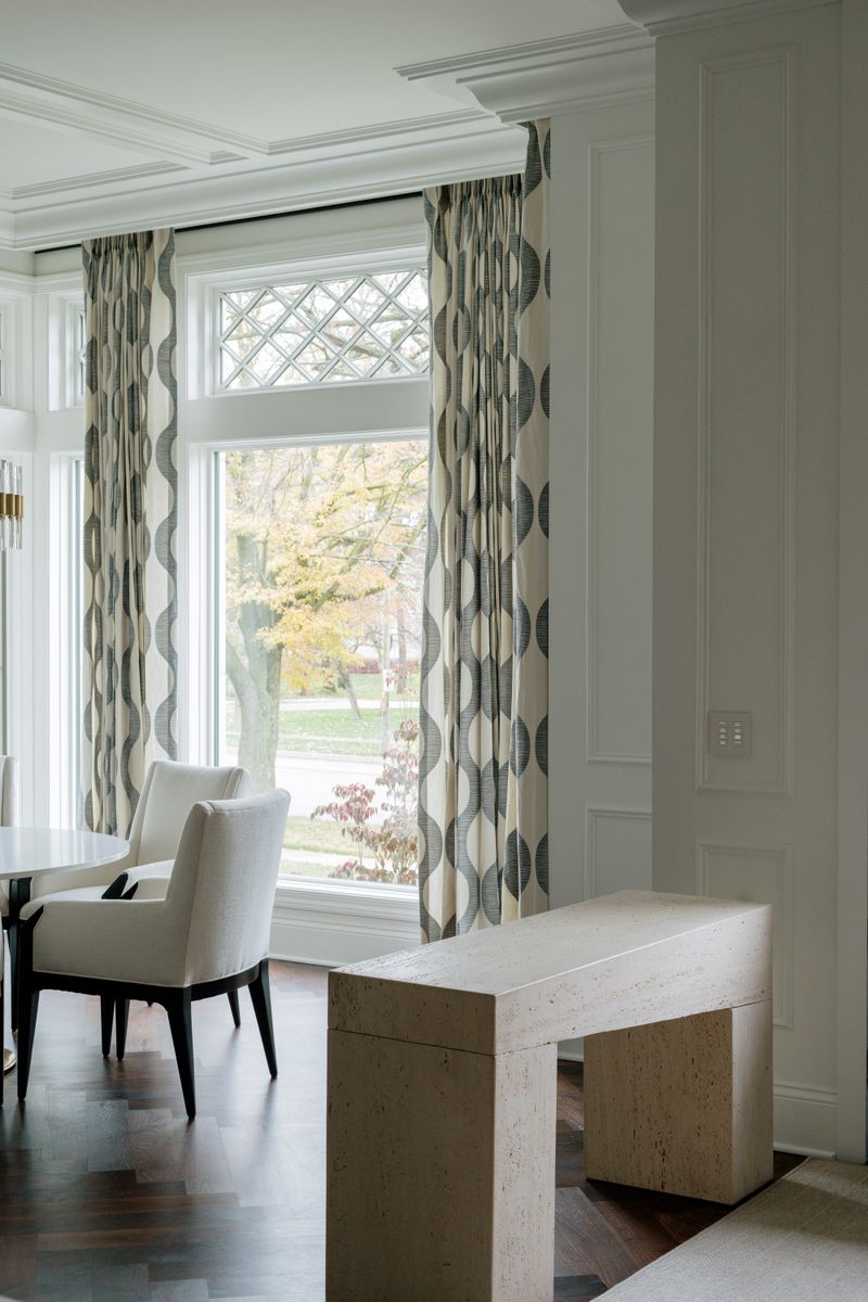 A dining room in Des Moines with a travertine console table beside patterned gray drapes.