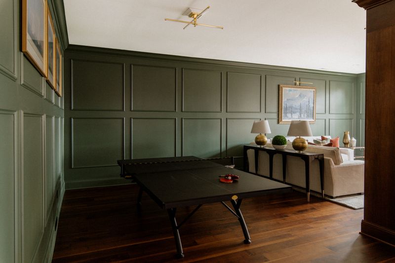 A game room in Des Moines with sage green paneled walls behind a black ping pong table on wood floors.