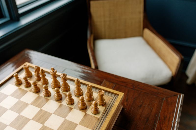 A game room in Des Moines with a wooden chess set on a dark walnut table by a black painted window.