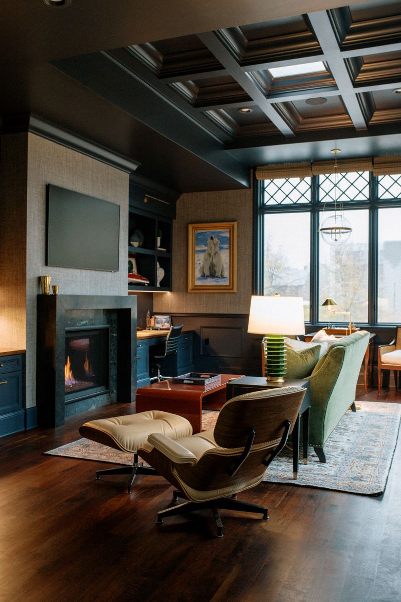 A moody home office in Des Moines with a dark coffered ceiling over a tan leather lounge chair.