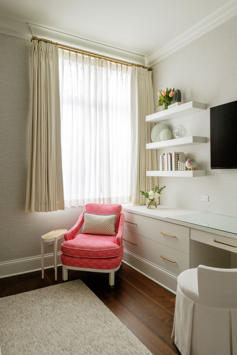 A home office in Des Moines with a pink patterned armchair beside white built-in cabinets with brass pulls.