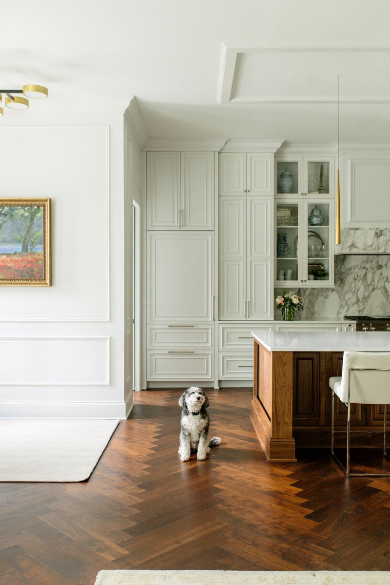 A soft white kitchen in Des Moines with a walnut island sitting on herringbone wood floors.