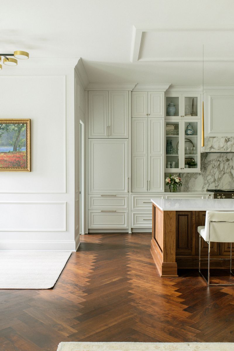 A cream kitchen in Des Moines with a walnut island set on herringbone wood floors.