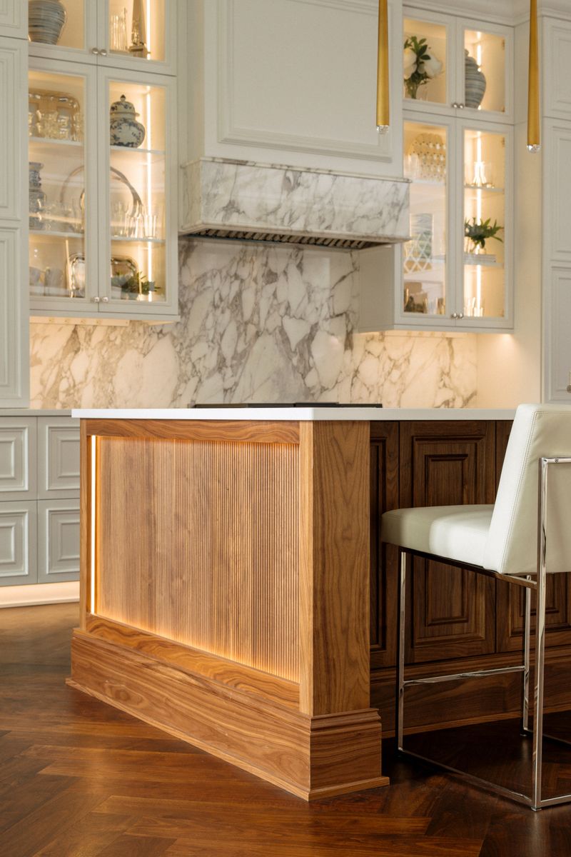 A Des Moines kitchen with a marble range hood above a fluted walnut island lit from within.
