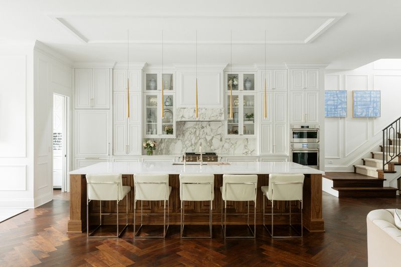 A white kitchen in Des Moines with a walnut island under a marble range wall, over herringbone wood floors.