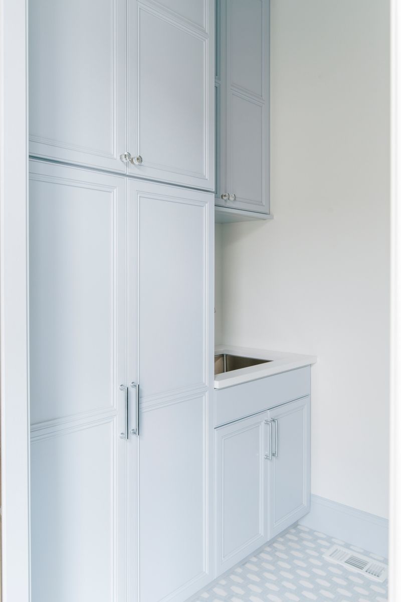 A pale blue laundry in Des Moines with glass knobs on floor to ceiling cabinets and a stainless sink.