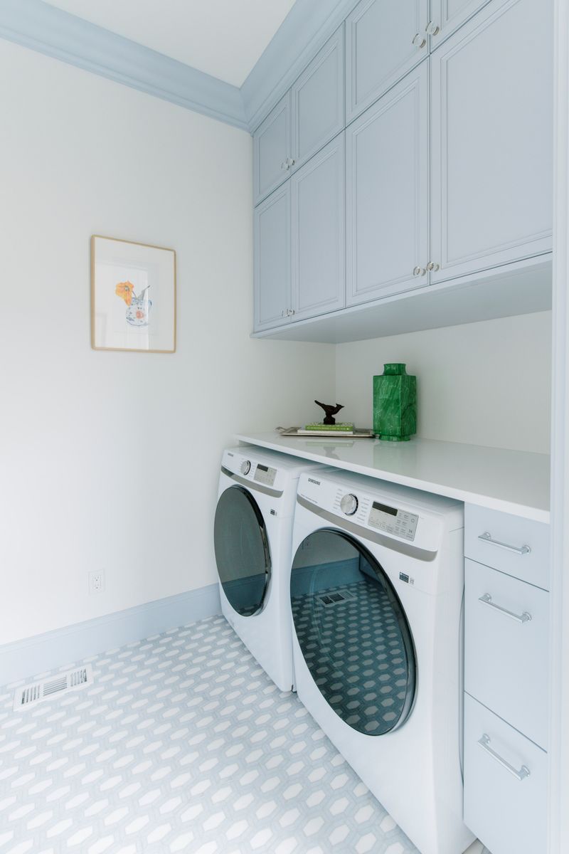 A pale blue laundry room in Des Moines with a white quartz counter over the washer and dryer and mosaic tile floors.