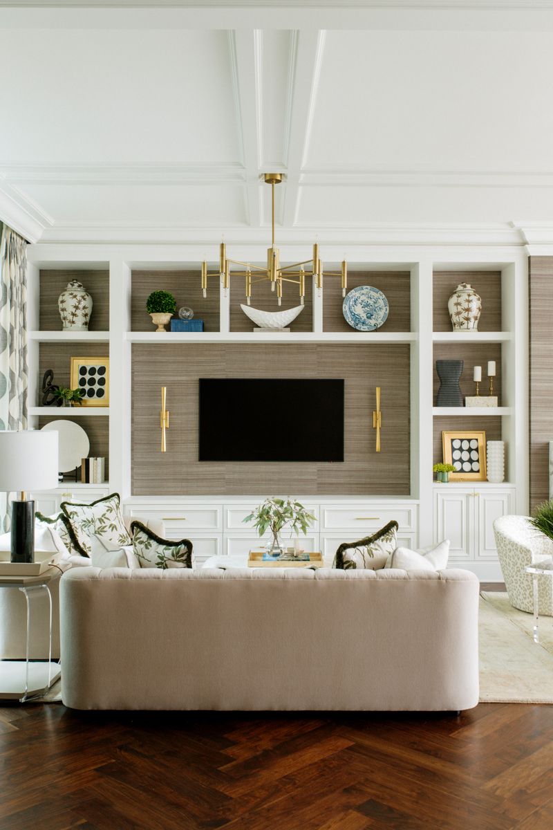 A living room in Des Moines with white built-ins around a grasscloth media wall and brass sconces.