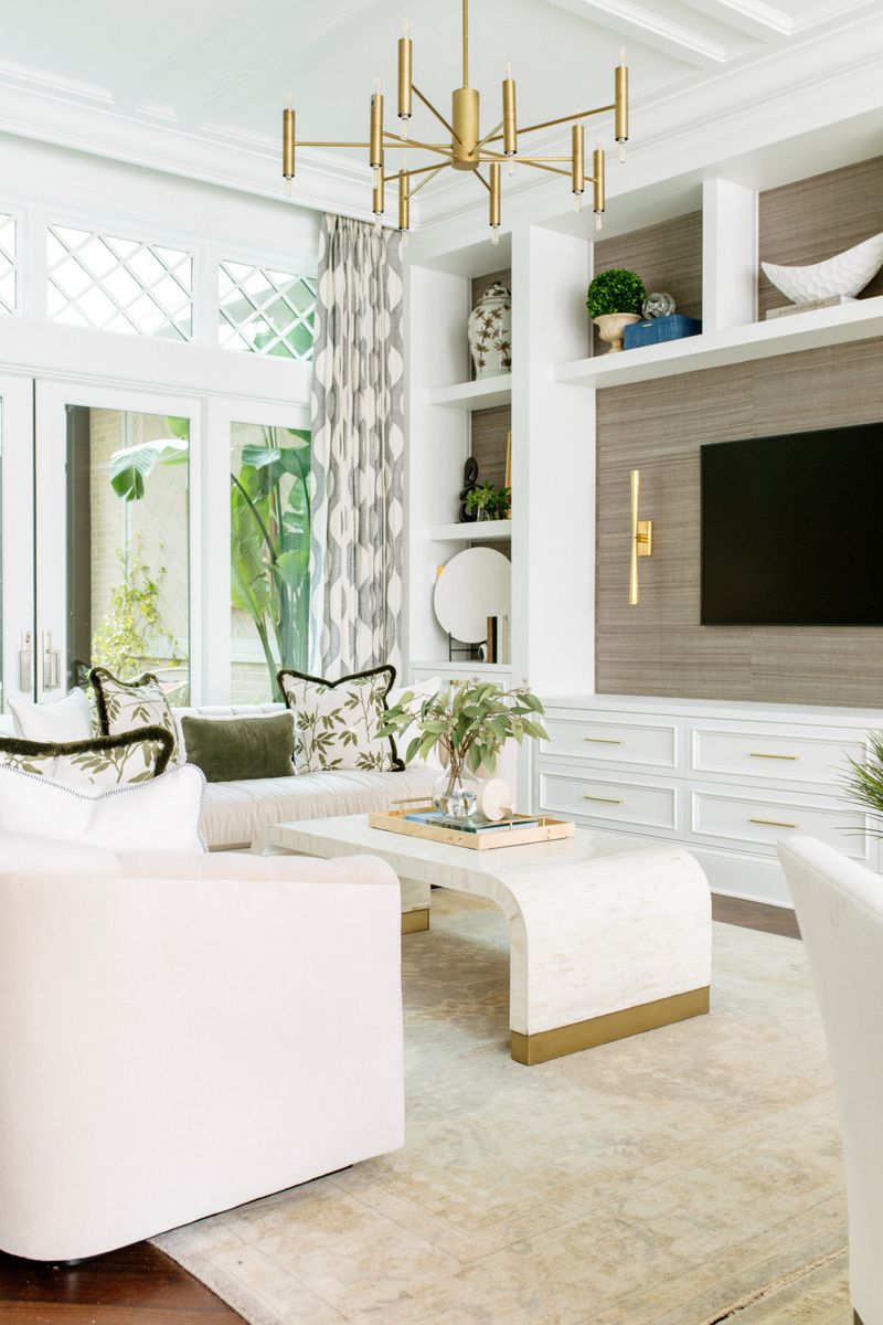 A white living room in Des Moines with a grasscloth media wall built into white cabinets with brass pulls.