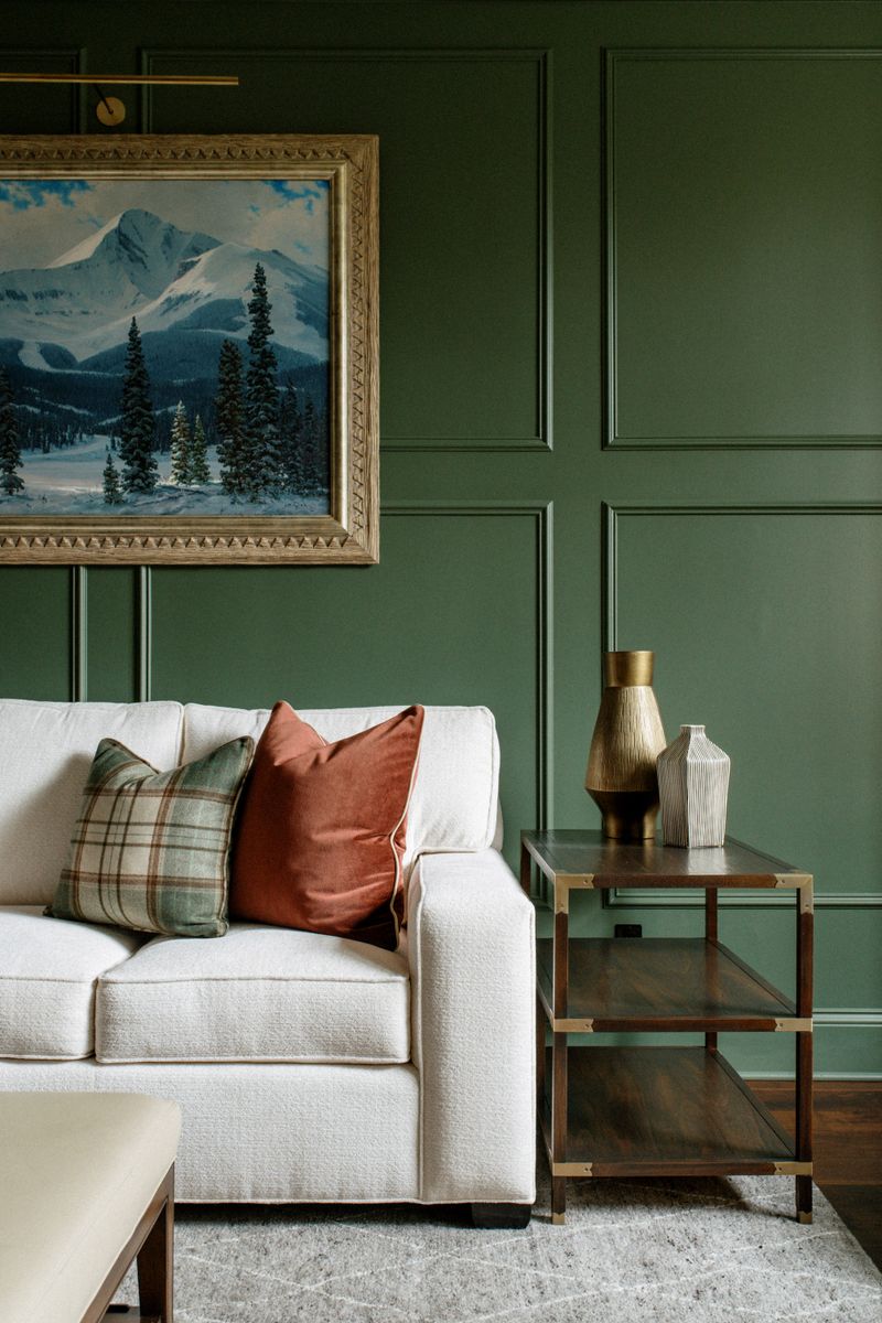 A living room in Des Moines with a green paneled wall behind a cream sofa and a walnut side table.