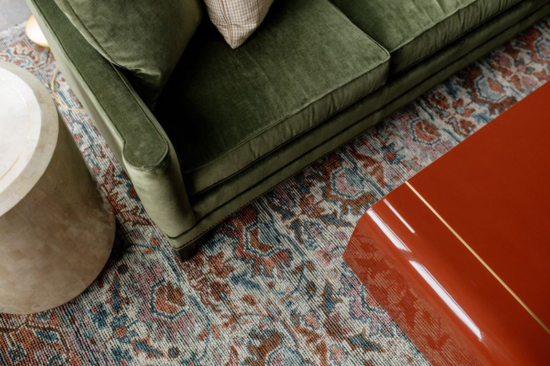 A Des Moines living room with a green velvet chair sitting on a faded blue and rust vintage rug.