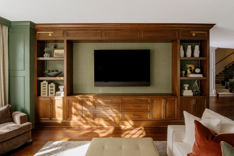 A living room in Des Moines with stained wood built-ins against a green grasscloth media wall.