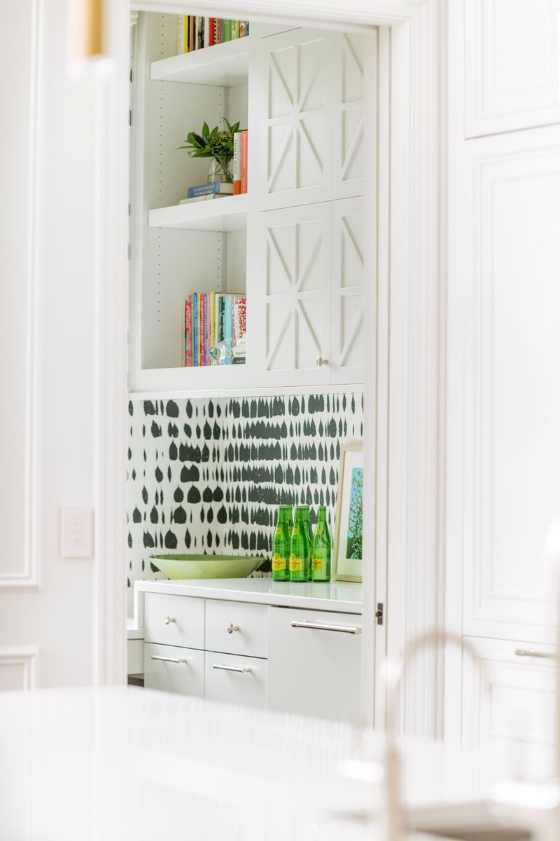 A white pantry in Des Moines with black brushstroke wallpaper behind the counter and glass front cabinets above.