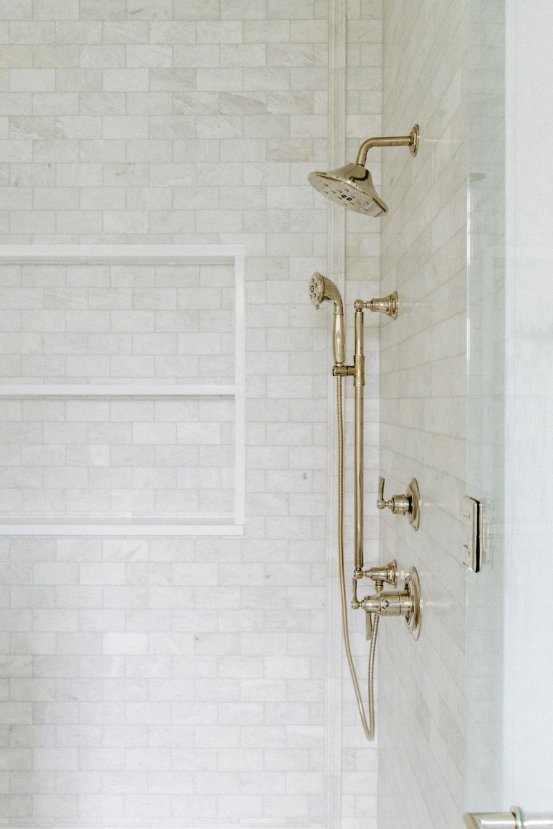 A primary bath shower in Des Moines with polished nickel fixtures on white marble subway tile and a built-in niche.