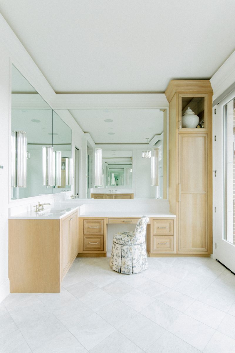 A primary bath in Des Moines with a white oak vanity and a floral skirted stool at the makeup counter.