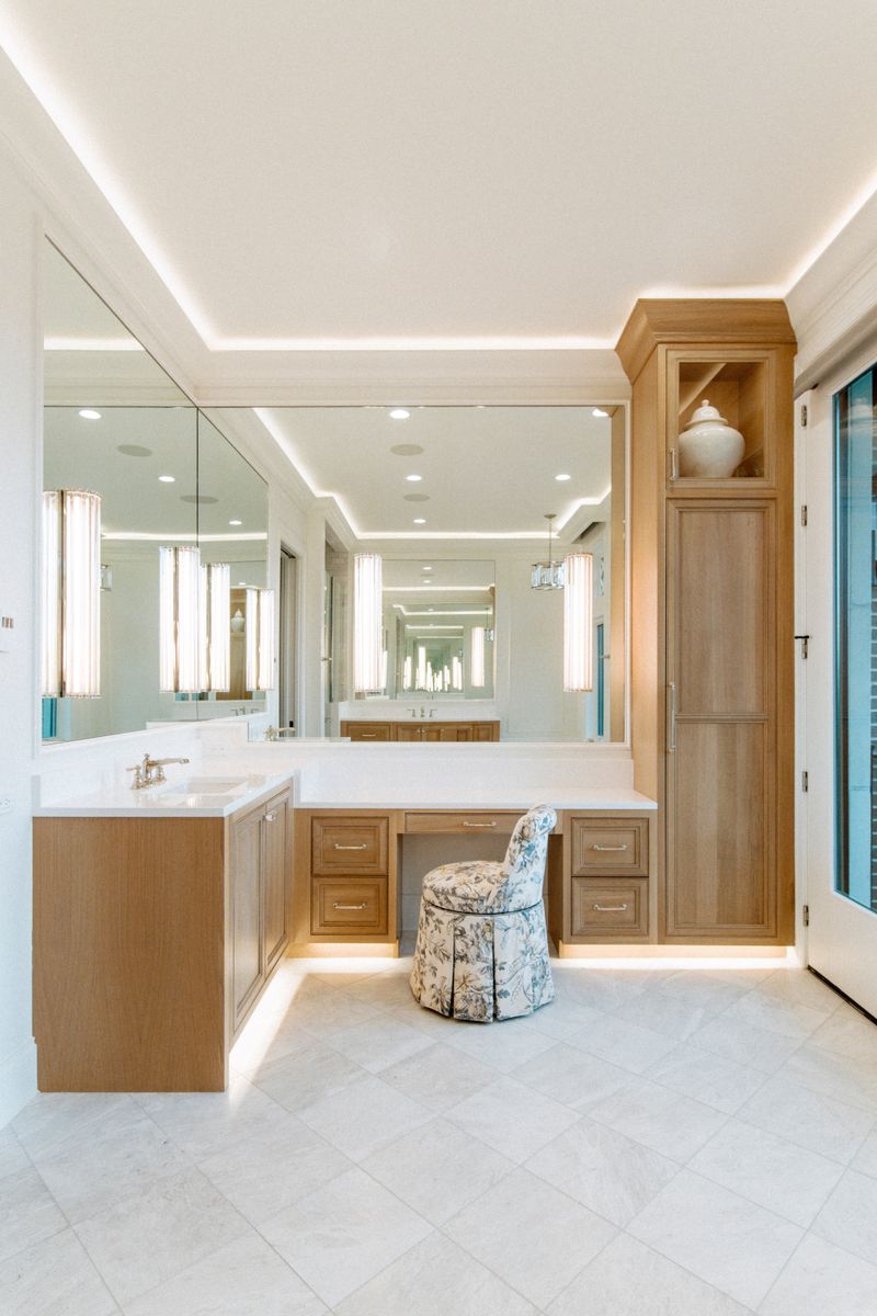 A primary bath in Des Moines with white oak vanity cabinets and a floral skirted stool at the makeup counter.